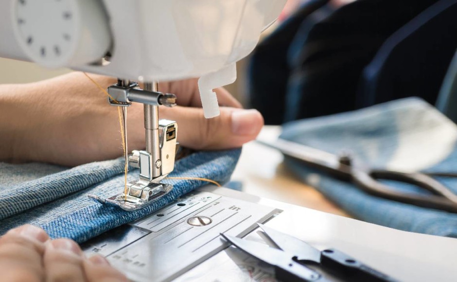 Manos de una mujer utilizando una máquina de coser como herramienta de trabajo para su negocio de corte y confección