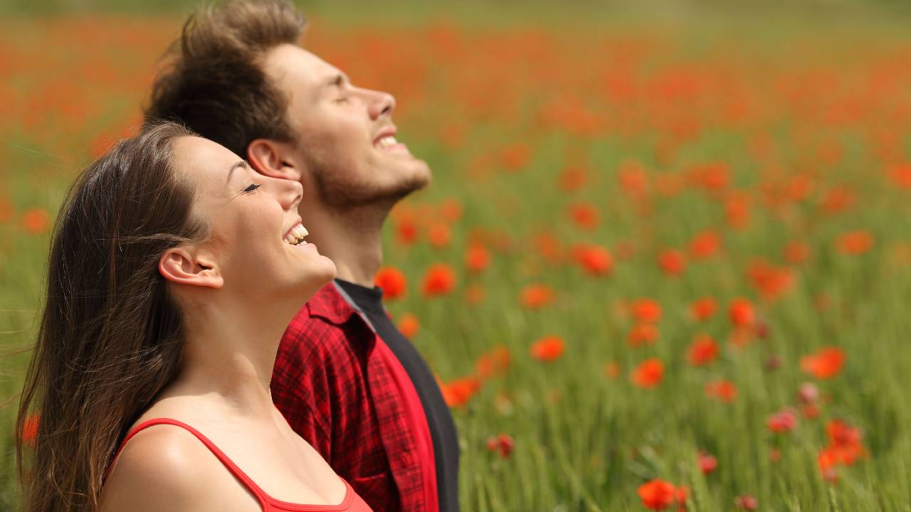 Pareja de hombre y mujer sonriendo frente a un campo de flores rojas