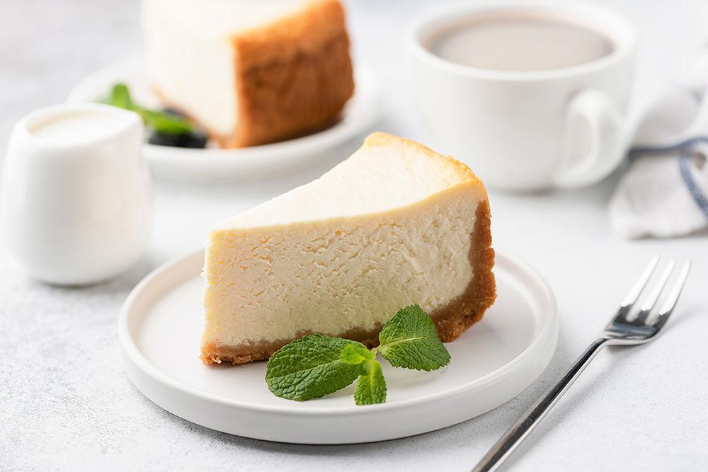 postre de queso sobre un plato blanco, rodeado de una taza de cafe