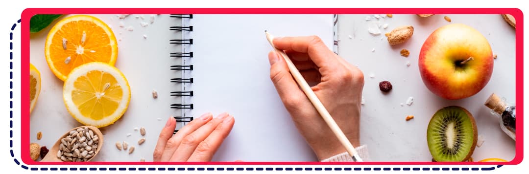 imagen de una mano tomando notas en un cuaderno junto a diversas frutas