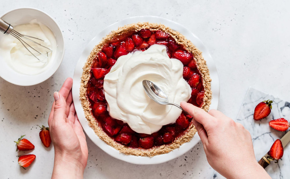 mano de una persona decorando una tarta de fresas con crema batida en la superficie