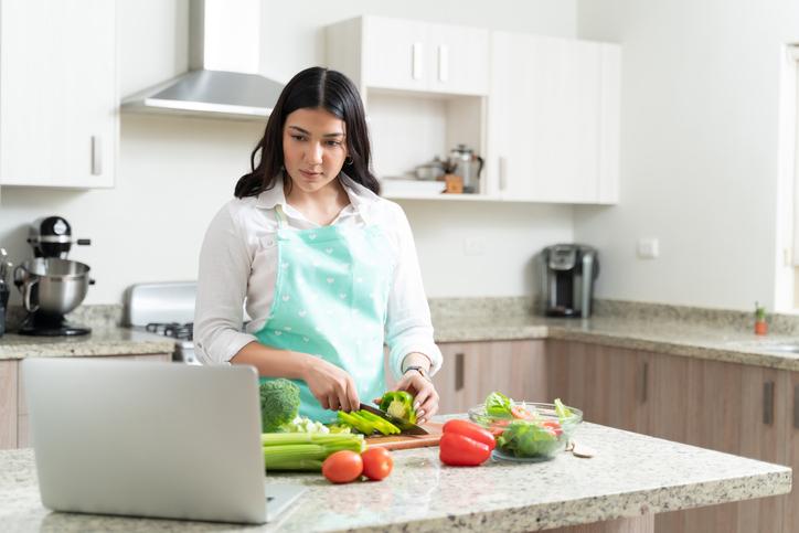 mujer cortando vegetales mientras aprende online