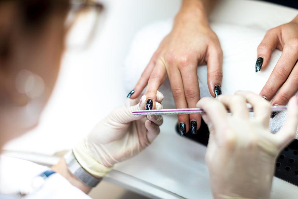manos de una manicurista arreglando las uñas de una mujer