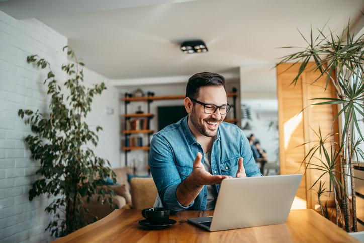 hombre sonriendo y haciendo un gesto con las manos mientras mira un computador