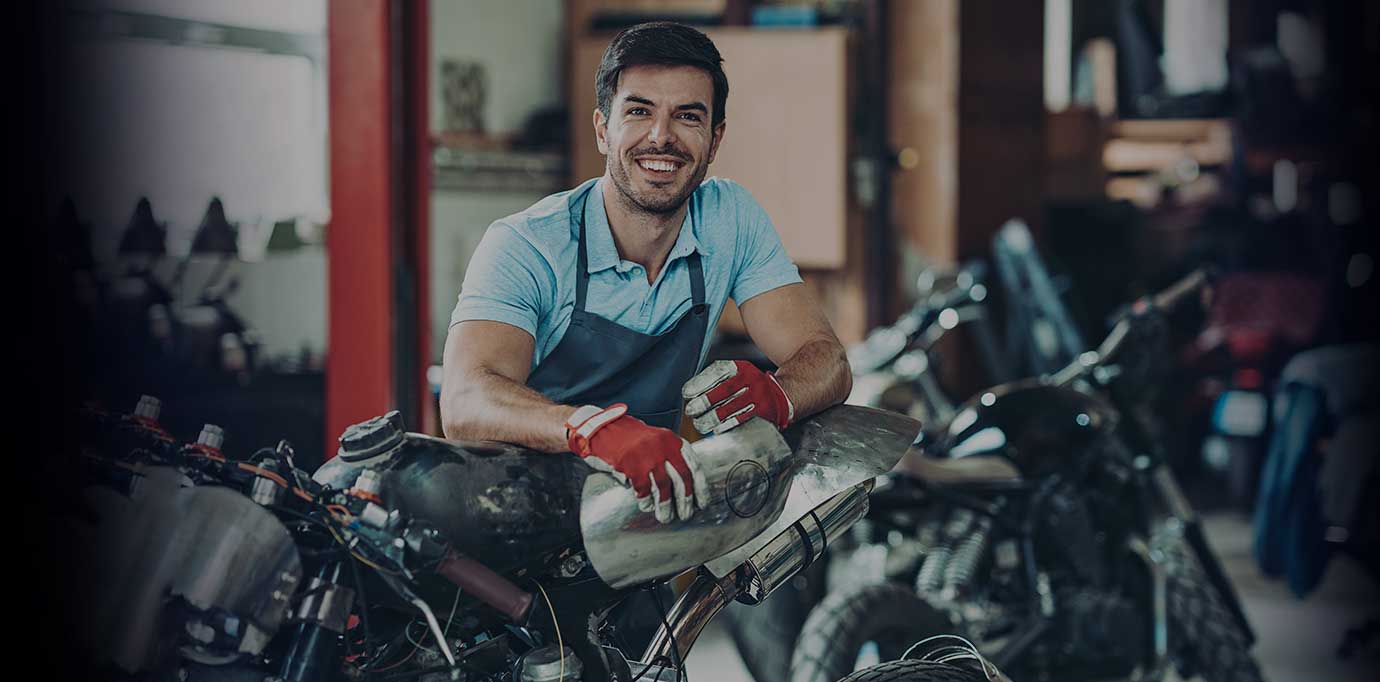 Mecánico profesional sonriendo posado sobre la parte trasera de una moto.