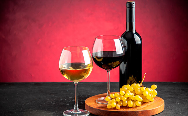 Botella de vino y copa sobre un barril donde se aprecie un racimo de uvas
